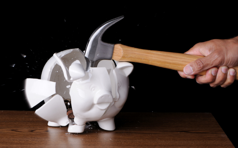 Hand holding hammer smashing a piggy bank